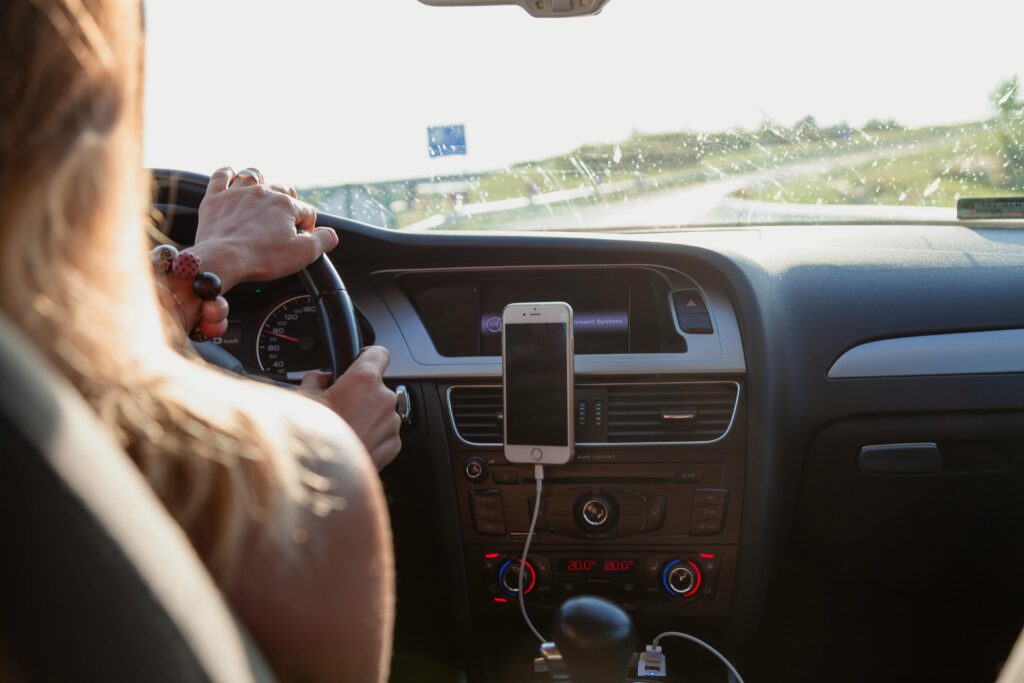 pexels-photo-1386649-1386649 View from behind a woman driving a car on a sunny day with a phone mounted on the dashboard.